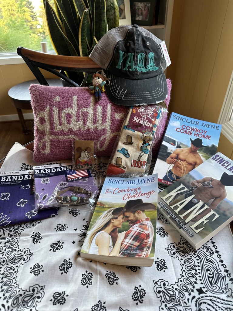 Photo of giveaway items that include three books, a "giddy up" throw pillow,  a hat, and some bandanas.